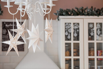 White Scandinavian paper stars in the Christmas decoration of the kitchen interior. The concept of preparation for the New Year holidays in 2024.