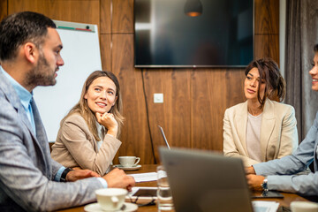 Colleagues at meeting in boardroom, sitting at table together, sharing ideas, discussing project strategy.