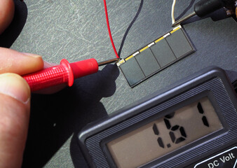 Tiny solar cell voltage test with multimeter under the sunlight. Photoelectric cells. Focused on cell. - obrazy, fototapety, plakaty
