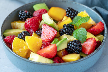 Healthy fruit salad in a grey bowl made with avocado, strawberry, raspberry, orange, blackberry, peaches. Close-up, grey background