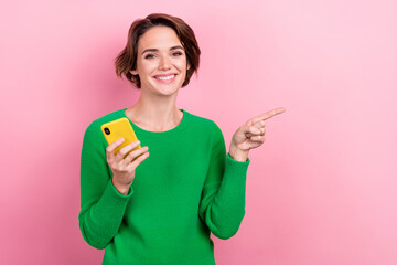 Photo of young internet user woman hold gadget directing finger empty space virtual reality advertisement isolated on pink color background