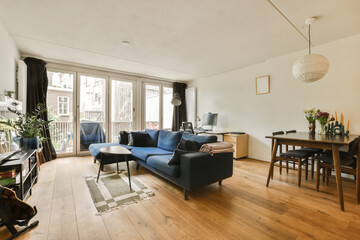 a living room with wood flooring and blue couch in the center of the room is a small dining table