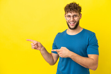 Young handsome caucasian man isolated on yellow background surprised and pointing side