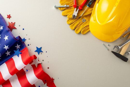 Capture attention with this construction-themed top-view image, showcasing a flag, work helmet, gloves, and tools on a light grey backdrop. Great for Labor Day campaigns, messages, or text placement