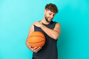 Handsome young man playing basketball isolated on blue background suffering from pain in shoulder...