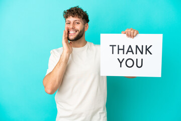 Young handsome caucasian man isolated on blue background holding a placard with text THANK YOU and...