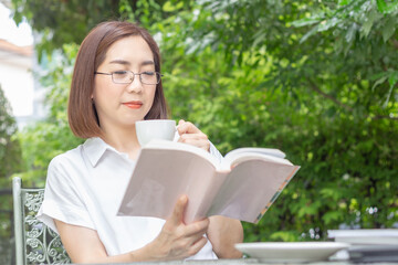Obraz premium Asian middle aged woman in glasses reading a book in backyard