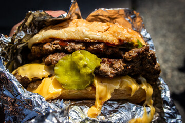 Messy hamburger with cheese and pickles wrapped in foil close-up