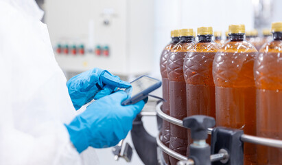 Factory worker woman with computer tablet inspecting production line with brown plastic bottles with beer. Concept brewery food industry