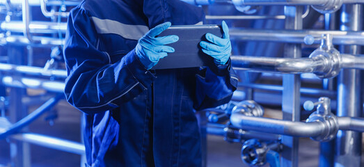 Factory worker inspecting production line with reservoirs or tanks on Brewery plant with computer tablet. Concept food industry banner