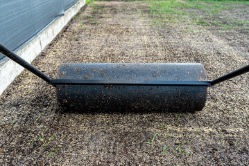 Rolling freshly sown grass seeds with a metal roller filled with water.