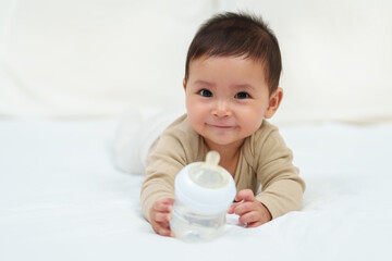 baby drinking water from bottle on bed