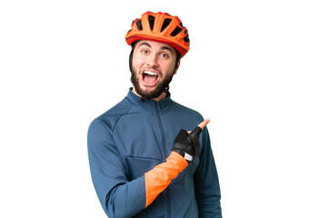 Young cyclist man over isolated chroma key background surprised and pointing side