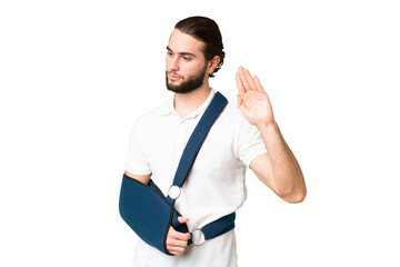 Young handsome man with broken arm and wearing a sling over isolated chroma key background making stop gesture and disappointed