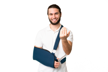 Young handsome man with broken arm and wearing a sling over isolated chroma key background inviting to come with hand. Happy that you came