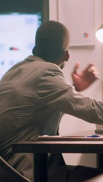Vertical video African american employee pissed about noisy coworker listening to music and pretending to beat drums in office. Businessman frustrated with overzealous colleague banging desk