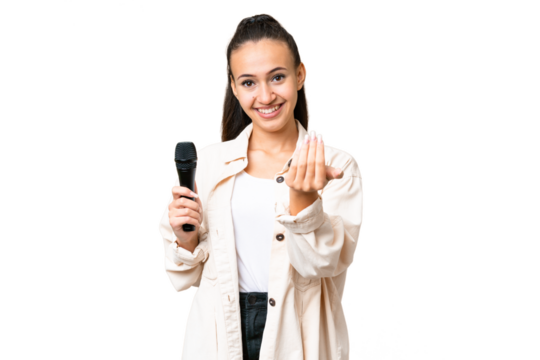 Young singer woman picking up a microphone over isolated chroma key background inviting to come with hand. Happy that you came