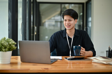 Fototapeta premium A happy Asian male marketing officer working on his project on his laptop at his desk.