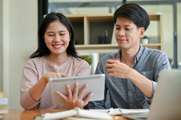 Two happy young Asian college students are looking at a tablet screen together, talking