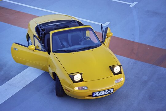 Auto mazda  model mx-5   1995 r. miata w kolorze sun burst yellow gen N po liftingu zaparkowana na parkingu widok z zewnątrz.