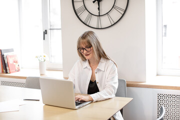 Woman works at a computer. Home office, scandinavian minimalist interior. Information Technology. Search for information on the Internet. Woman with glasses looks at a laptop screen.