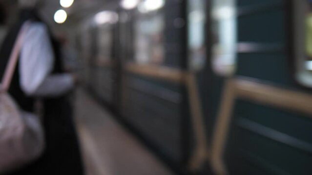 A blurry image of a subway train approaching a station full of people. People are waiting for the subway train.
