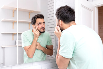 Young funny man with bugged eyes looking at the mirror after morning routine in the bathroom	