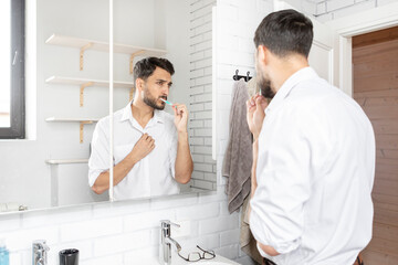 Handsome businessman brushing teeth in the bathroom. Morning routine concept
