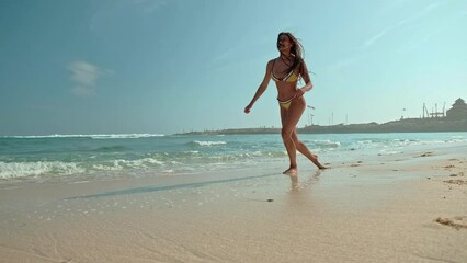 Beautiful young woman in yellow bikini jumping on the beach at sunny day in summer. Side view of beautiful female jumping at beach on a sunny day Tropical landscape. Sexy back of slim girl, clear
