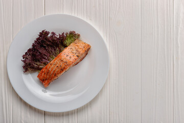 Fried piece of salmon fillet with salad leaf, on a white plate, on a white wooden board