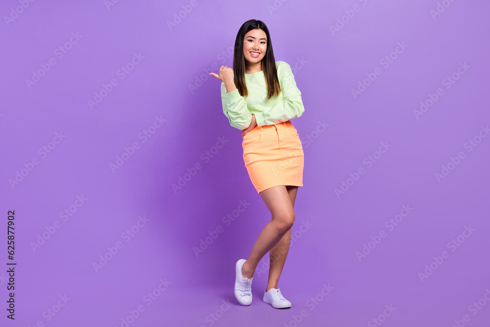 Sticker Portrait of satisfied gorgeous girl wear stylish pullover skirt indicating at offer empty space isolated on violet color background