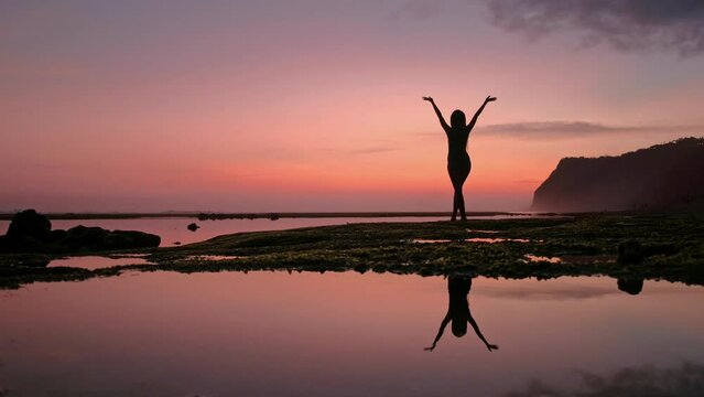 Silhouette of Woman Raising His Hands or Open arms when sun rising up. A young slim mindful female does yoga by the sea. Peaceful girl standing pose with her raising hands up to greet the dawn
