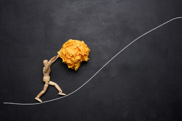 A wooden figurine of a person rolling a crumpled paper ball upwards, concept of perseverance and hard work, achieving goals. - obrazy, fototapety, plakaty
