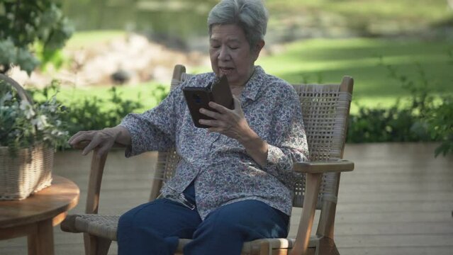 asian old elderly senior elder woman talking using video chat on smart mobile phone in garden
