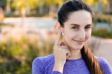 portrait of a woman in purple sportswear touching headphone and smiling to the camera