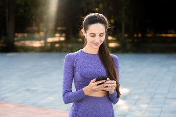 woman in purple sportswear smiling and searching the music in phone
