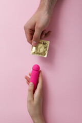 A condom with a vibrator in hands on a pink background - obrazy, fototapety, plakaty