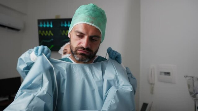 Assistant helps the surgeon to don the sterile gown