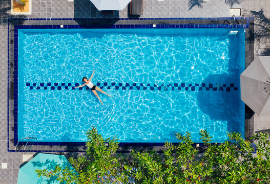 Young female in white swimsuit relaxing in swimming luxury villa swimming pool. Aerial top view shot. Careless summer vacation concept image.