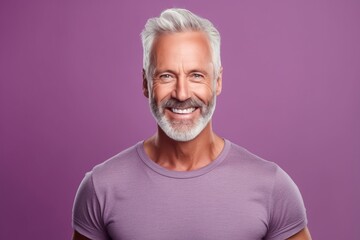 Portrait of a handsome mature man with grey hair and beard looking at camera and smiling while standing against purple background