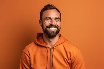 Tuinposter smiling man in orange hoodie looking at camera isolated on orange © igolaizola