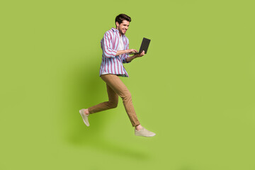 Photo of cheerful funny man dressed striped shirt holding laptop typing email hurry running shopping isolated on green color background