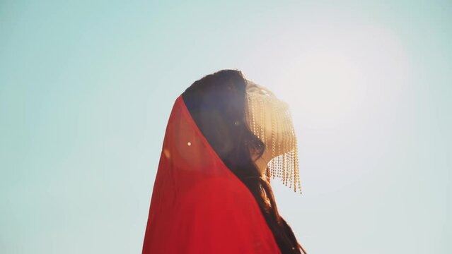 portrait young happy arabian woman enjoy life sun light freedom summer nature desert. oriental gold metal chain golden mask hides face red silk scarf covers head sexy fashion model girl luxury style