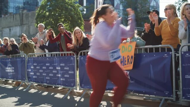 Diverse Group of People Running a Marathon in a City During the Day. Zoom in on Supportive Family Members in the Family: Little Girl and her Mother Cheering for her Dad in the Audience