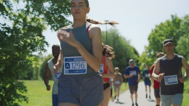 Slow Motion Portrait of a Woman Running and Participating in a Marathon in a Park. Strong Athletic Female Jogger Racing Other Runners with Determination for the First Place in the Finish Line