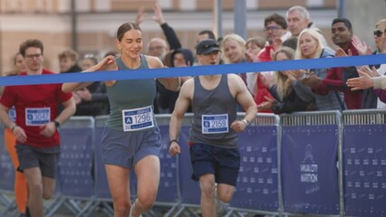 Slow Motion Portrait of Athletic Female Jogger Crossing the Finish Line in Marathon Race with the Audience Cheering. Happy Successful Woman Celebrating Winning, Feeling Empowered with her Achievement