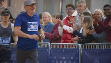 Slow Motion Portrait of a Senior Male Jogger Running in a City Marathon and Being Cheered for by the Audience. Healthy and Fit Elderly Man Enjoying Physical Activity and Staying in Shape