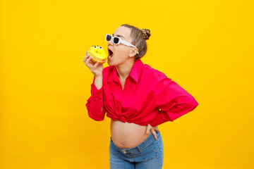 Positive pregnant woman eating donuts wearing pink shirt isolated on yellow background. Happiness from pregnancy while expecting a child. High quality photo. Harmful food during pregnancy