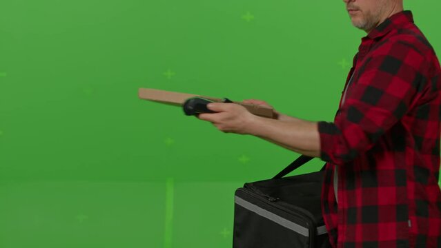 Caucasian male courier passing a box of pizza on green screen chroma key background. Man hold wireless bank payment POS terminal to process acquire credit card payment. Copy space mock up advertising