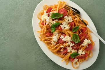 Salad caprese or pasta spaghetti broken with basil and mozzarella ala caprese on white plate on green rustic wooden background. Traditional Italian cuisine. Italian food concept. Top view. Recipe.
